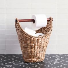 a wicker basket with two rolls of toilet paper in it on a tiled floor