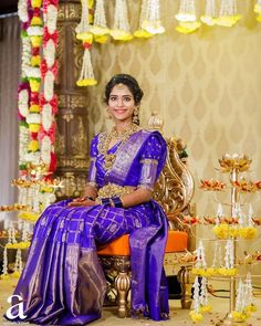 a woman sitting on top of a chair in a purple sari and gold jewelry