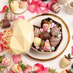 chocolate covered strawberries in a heart shaped box on a plate with pink flowers around it