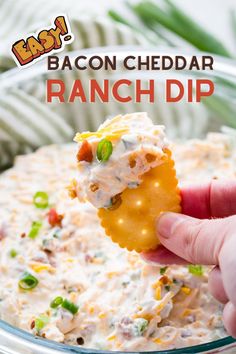 bacon cheddar ranch dip in a glass bowl with a hand holding a cracker