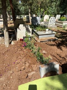 an old cemetery with several headstones and flowers in the dirt near some trees on a sunny day