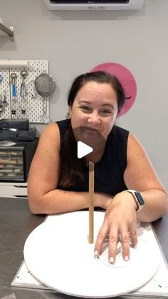 a woman sitting at a table in front of a white plate with a wooden stick sticking out of it