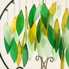 a wind chime with green and yellow leaves hanging from it's sides on a metal stand