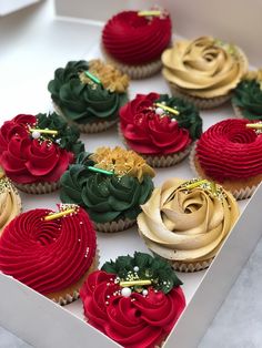 cupcakes decorated with red, green and gold icing in a white box