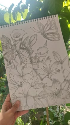 a person holding up a drawing in front of some trees and bushes with butterflies on it