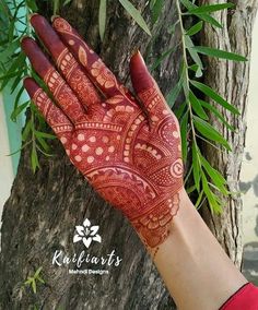 a woman's hand with henna on it and green leaves in the background