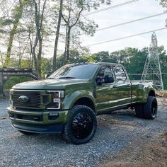 a large green truck parked on top of a gravel road next to trees and power lines