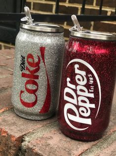 two glitter soda cans sitting next to each other on top of a brick floor covered ground