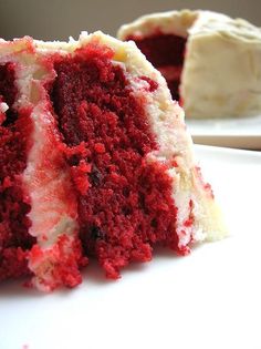 a piece of red velvet cake with white frosting on a plate next to another slice