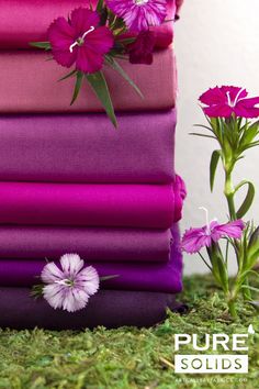 a stack of purple and pink sheets with flowers in the corner next to them on green grass