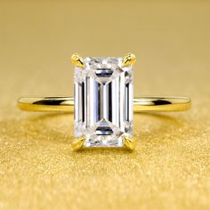 an emerald - cut diamond ring sits on a gold surface