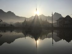 the sun shines brightly through the foggy sky over a lake in front of some mountains