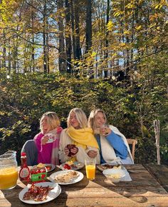 three women sitting at a picnic table with food and drinks in front of them on a sunny day