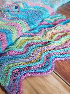 a multicolored crocheted blanket laying on top of a wooden floor