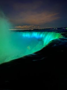 the niagara falls lit up at night with green lights on it's sides and blue water