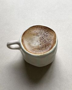 a cappuccino sitting in a white cup on a gray surface with its saucer