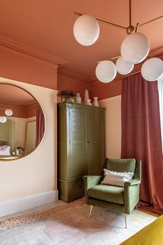 a green chair sitting in front of a mirror on top of a wooden dresser next to a window