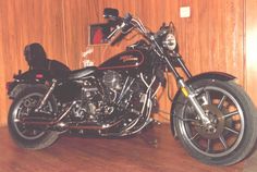 a black motorcycle parked on top of a wooden floor next to a wood paneled wall