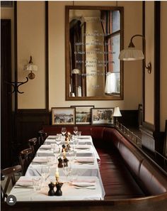 a long dining table with place settings and candles on it in front of a mirror