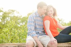 a man and woman sitting next to each other on a stone wall in front of trees