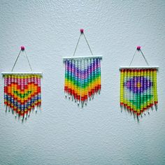 three colorful beaded hangings on a wall with pins attached to them and beads in the shape of hearts