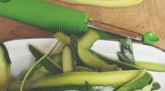 a bowl filled with sliced up cucumbers on top of a wooden table next to a banana peeler