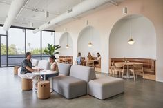 two people sitting on couches in a large room with lots of windows and tables