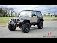 a gray jeep parked on top of a parking lot next to a grass covered field