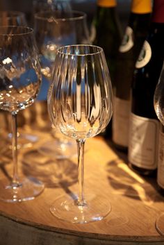 three wine glasses sitting on top of a wooden table next to bottles and glassware