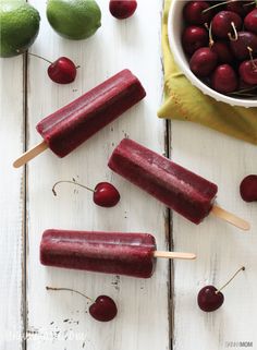 cherry popsicles with cherries on a white wooden table next to a bowl of cherries