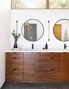 two round mirrors on the wall above a double sink vanity in a white bathroom with wood cabinets