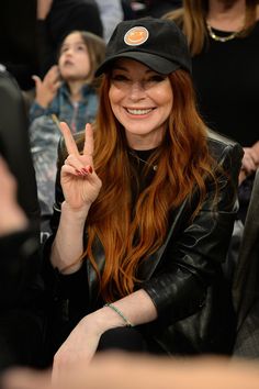 a woman with long red hair wearing a black hat and holding up her peace sign