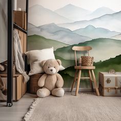 a teddy bear sitting in front of a wall mural with mountains on the back ground