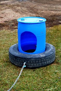 a blue barrel sitting on top of a tire in the grass next to a chain