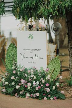 a wedding ceremony sign surrounded by flowers and greenery