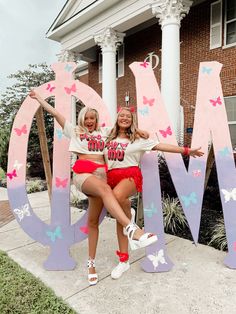 two girls are posing in front of the word mom with butterflies on it and one girl is holding her arms out