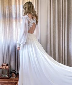 a woman in a white wedding dress looking out the window with her back to the camera