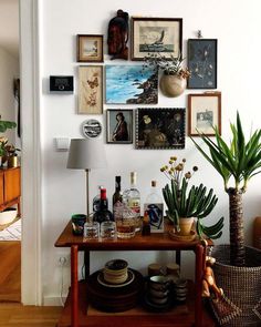 there is a table with bottles and glasses on it in front of a wall full of pictures