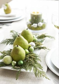 the table is set with white plates and silverware, green pears and greenery