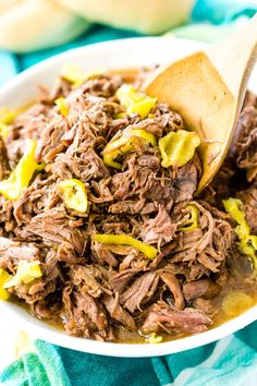 a white bowl filled with shredded beef and yellow peppers on top of a blue towel