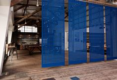 a room divider with blue perfored panels on the wall and wooden floors