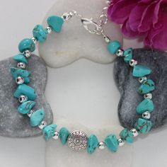 a bracelet with turquoise stones and silver beads on it next to a rock, pink flower and purple peonie