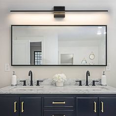 a bathroom vanity with two sinks and a large mirror above it, in front of a white wall