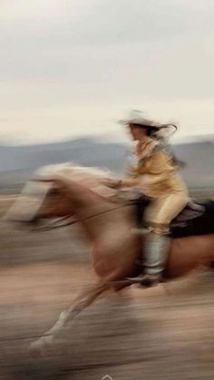 a man riding on the back of a brown horse across a desert field with mountains in the background