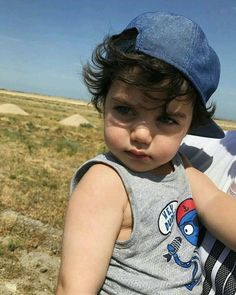 a little boy wearing a blue hat standing next to a man in a field with grass and rocks