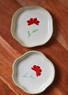 two plates with red flowers painted on them sitting on a wooden table next to each other