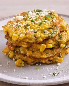 a stack of corn fritters on a plate topped with cheese and parsley