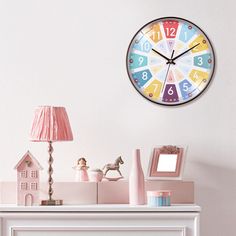 a clock on the wall above a dresser with pink lamps and other items in front of it