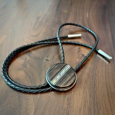 a black leather cord with a silver disc on it sitting on top of a wooden table