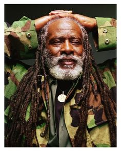 an older man with dreadlocks and a green camo jacket is holding his hands on his head